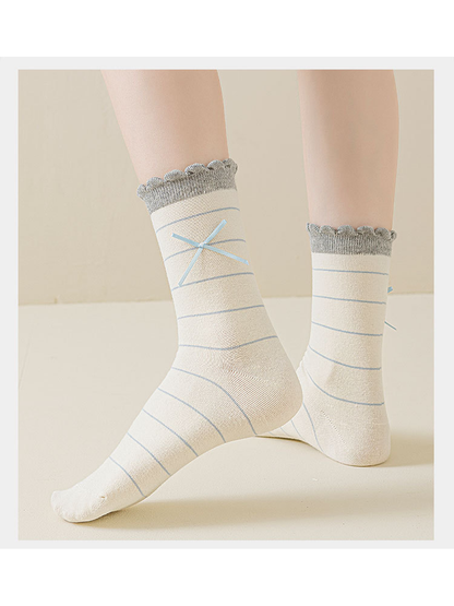 Ivory socks with pale blue stripes, ribbon bows, and scalloped gray cuffs worn without shoes.