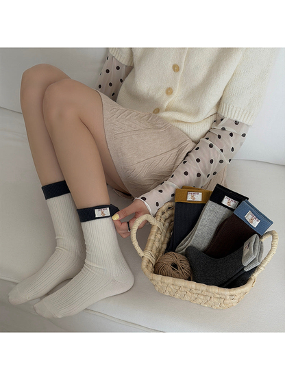 Ivory ribbed socks worn while seated beside a basket containing the other colors.