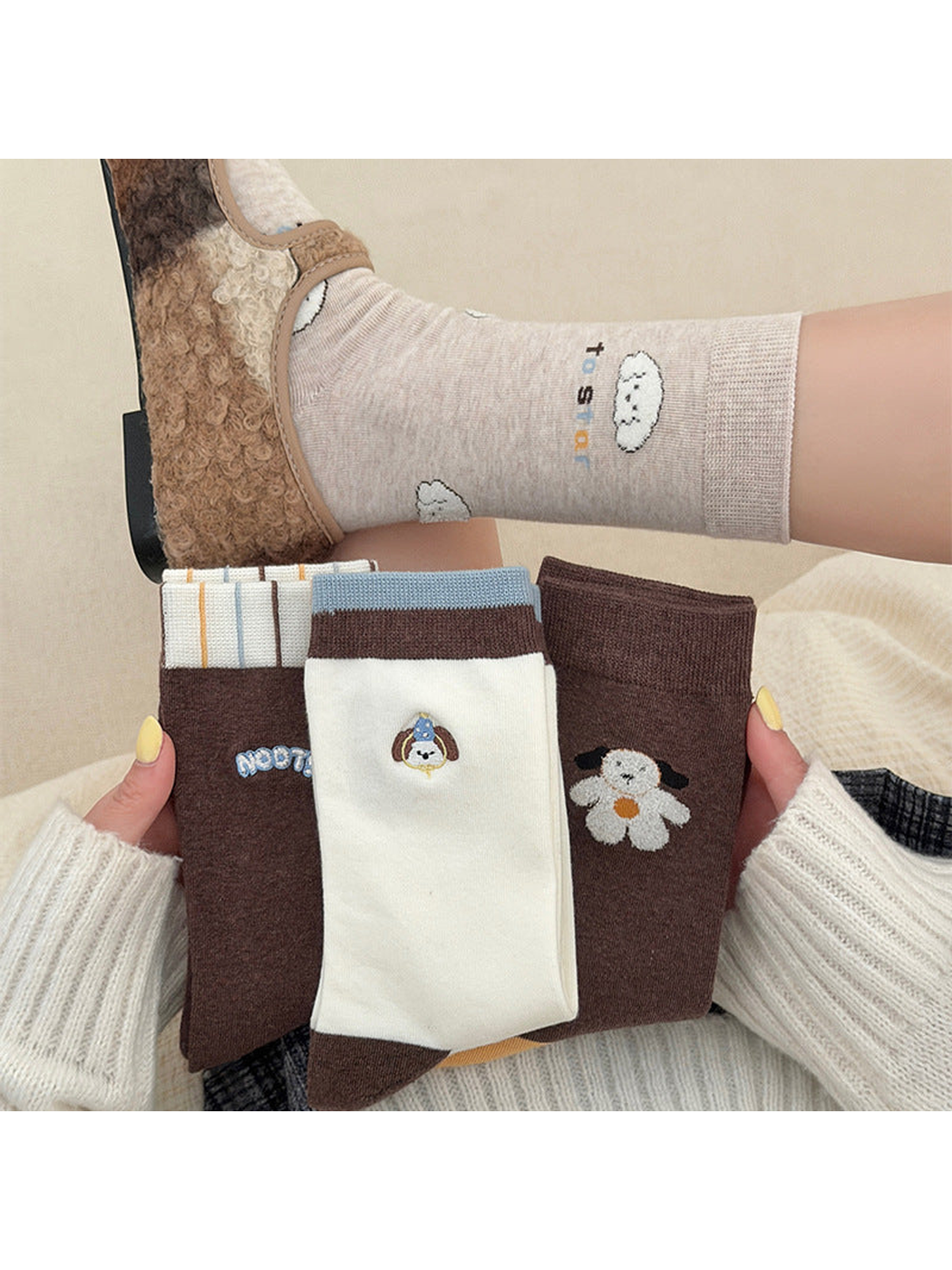 Folded socks with contrasting cuffs and dog motifs held below a worn Beige sock
