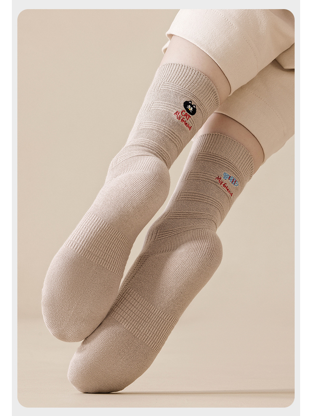 Beige cat and fish embroidered socks worn with crossed feet, showing the toes and knit texture.