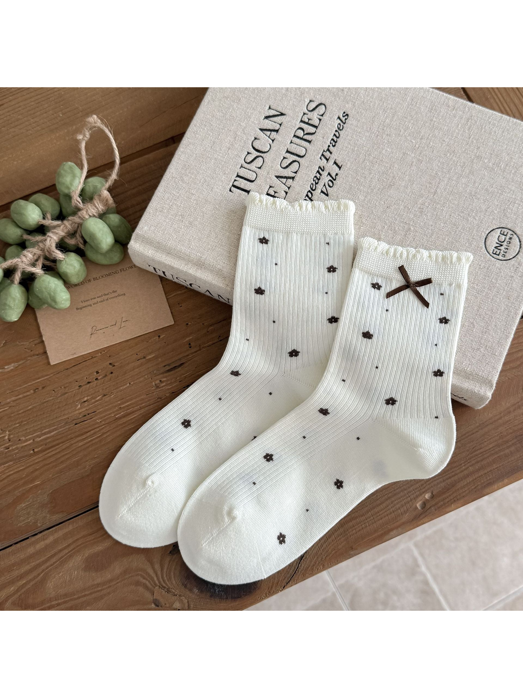 Floral socks in ivory with dark flower motifs, ruffled cuffs, and a brown bow.