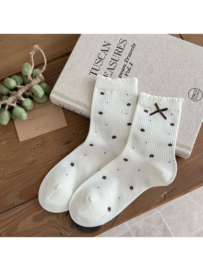 Floral socks in ivory with dark flower motifs, ruffled cuffs, and a brown bow.