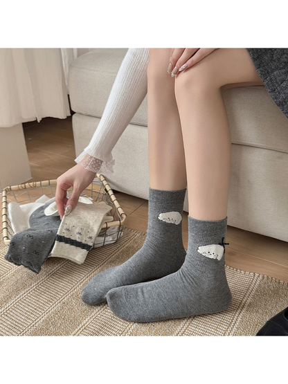 Gray Cartoon Applique socks worn beside a sofa, with white character motifs and black bows.