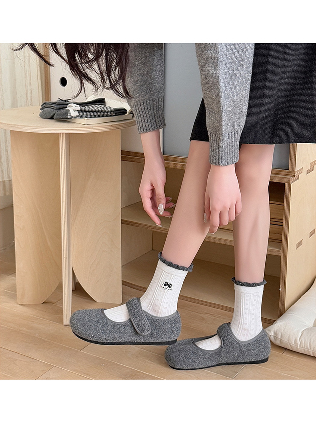 White Cartoon Face socks with dark ruffled cuffs worn with gray strap shoes while bending forward.