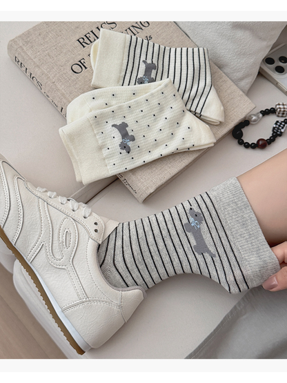 Gray striped dog motif sock worn with a white sneaker beside folded dotted and striped socks.