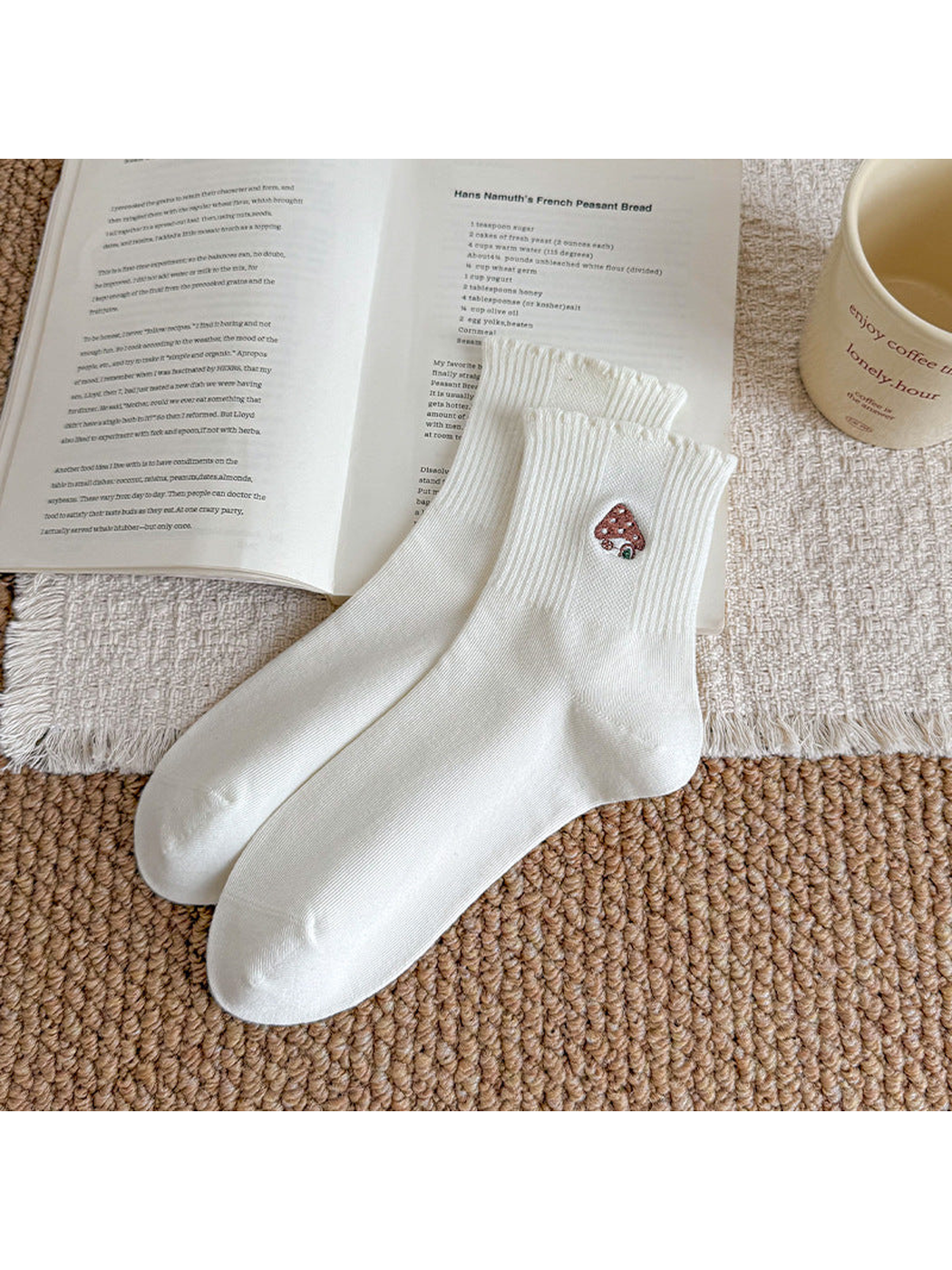 Ivory socks with mushroom-house embroidery and ribbed cuffs, arranged beside an open book.