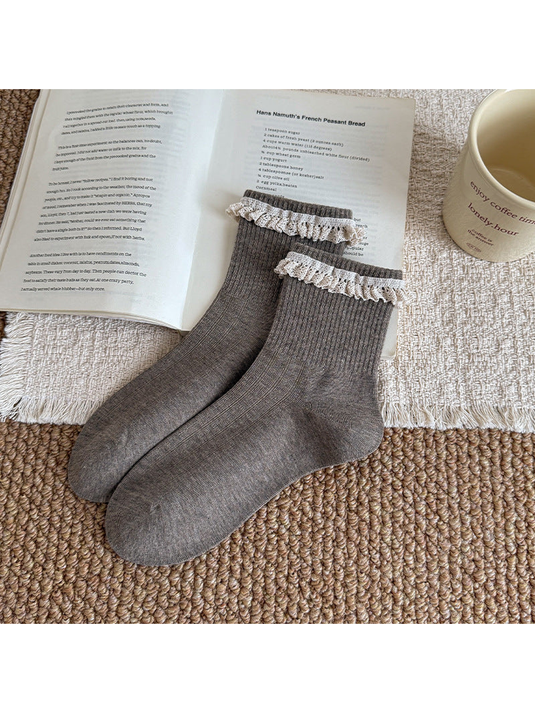 Gray ribbed socks with white lace ruffles at the cuffs, arranged beside an open book.