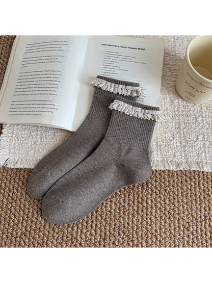 Gray ribbed socks with white lace ruffles at the cuffs, arranged beside an open book.