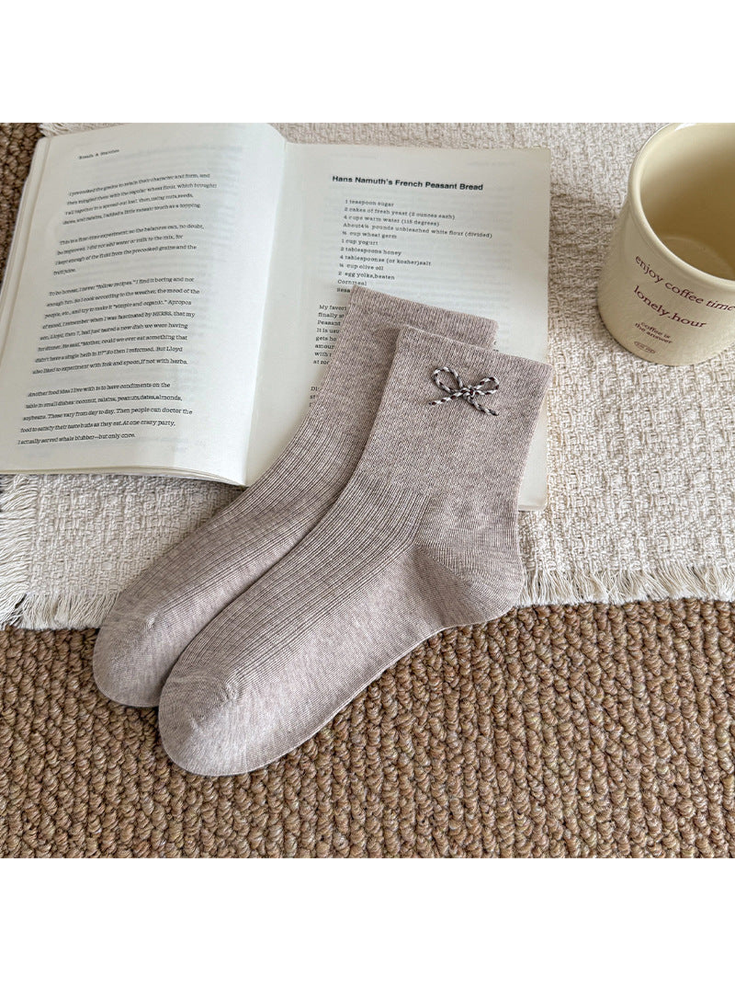 Beige ribbed socks with a contrasting cord bow near the cuff, arranged beside an open book.