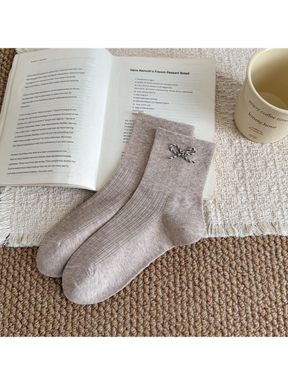 Beige ribbed socks with a contrasting cord bow near the cuff, arranged beside an open book.