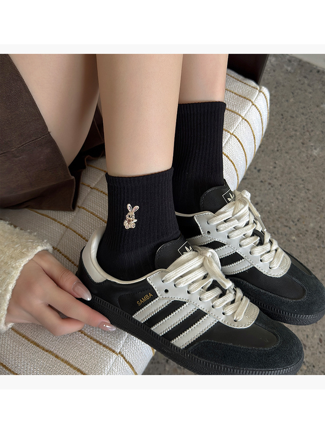 Black ribbed socks with rabbit embroidery worn with black and white lace-up sneakers.