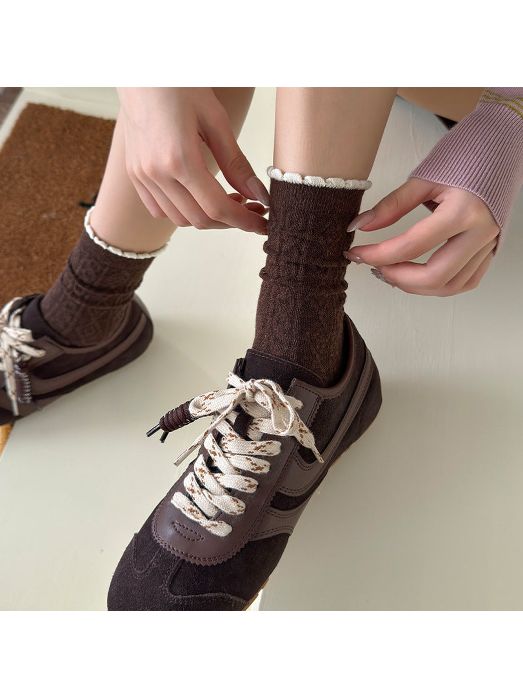 Hands adjusting brown socks with contrasting scalloped cuffs, worn with brown sneakers.