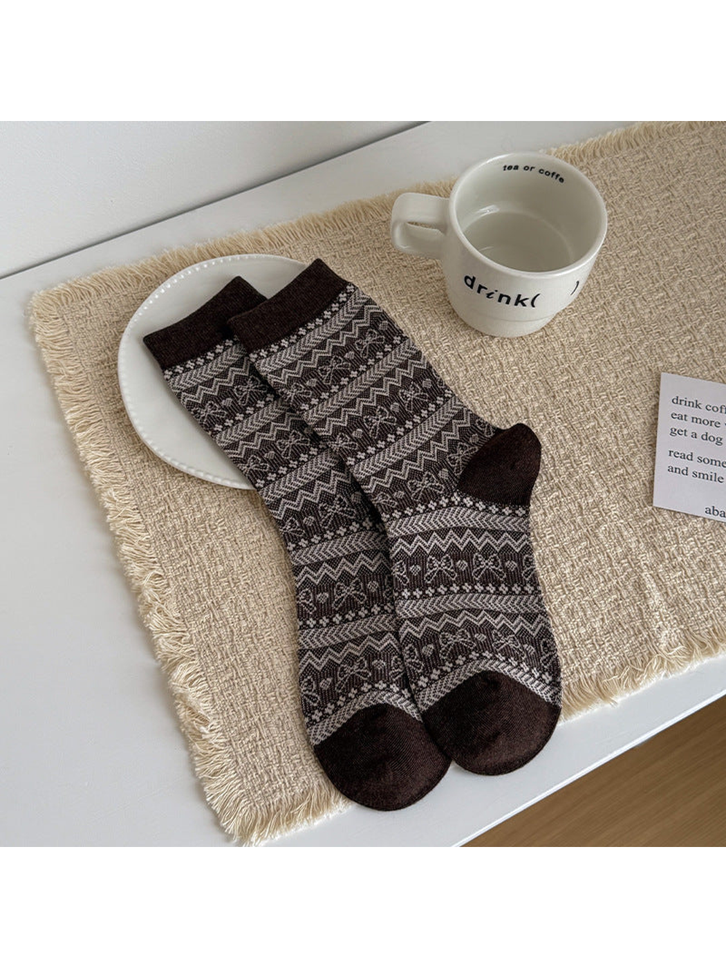 Fair Isle socks with brown cuffs, heels and toes, laid flat beside a cup.