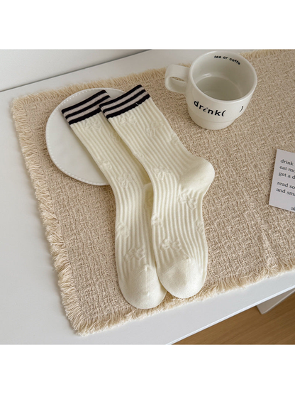Ivory Cable socks with brown cuff stripes, laid flat beside a cup.