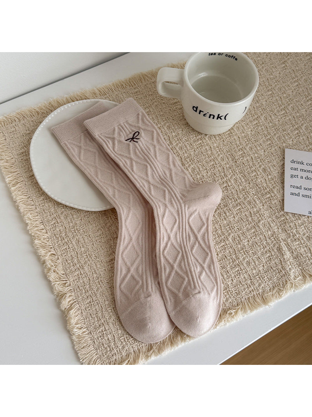 Beige Bow socks with diamond cable texture and a small embroidered bow, laid flat.