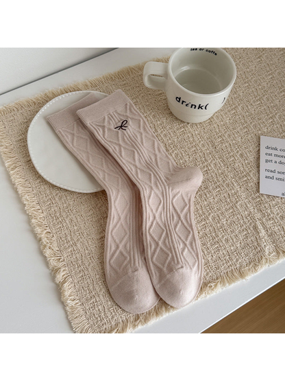 Beige Bow socks with diamond cable texture and a small embroidered bow, laid flat.