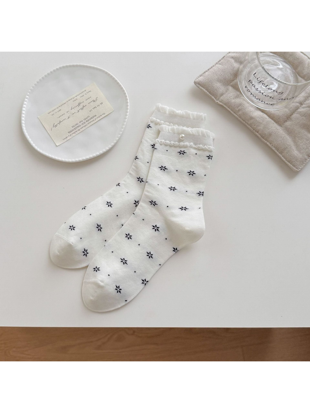 White socks with black floral motifs, ruffled cuffs and a round bead accent arranged on a tabletop.