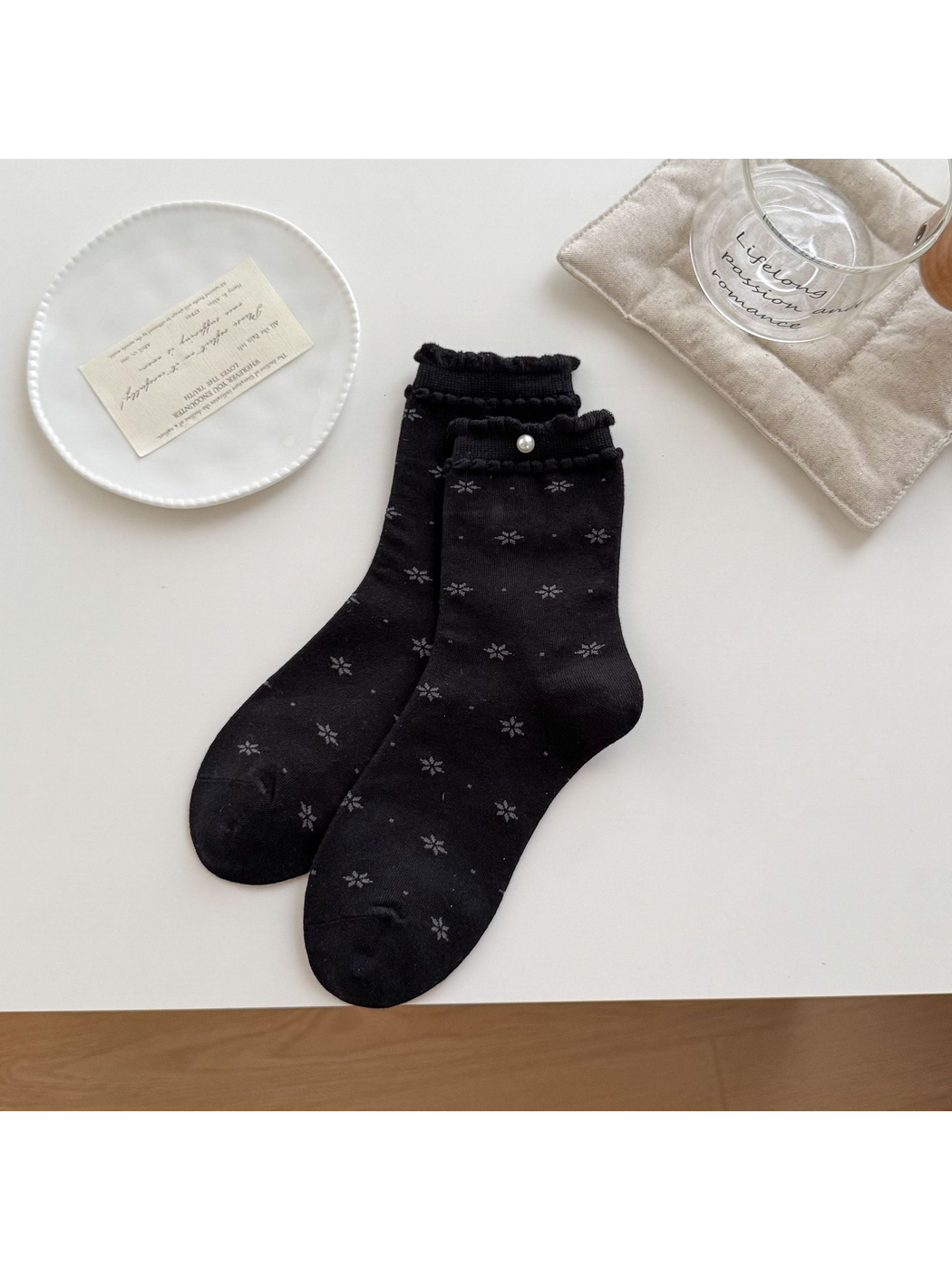 Black socks with gray floral motifs, ruffled cuffs and a round bead accent arranged on a tabletop.