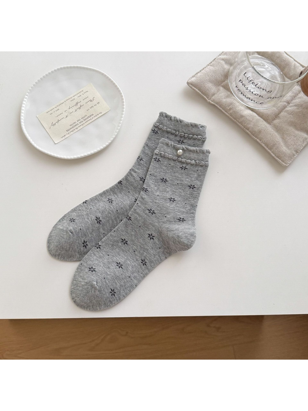 Light Gray floral socks with ruffled cuffs and a round bead accent arranged on a tabletop.