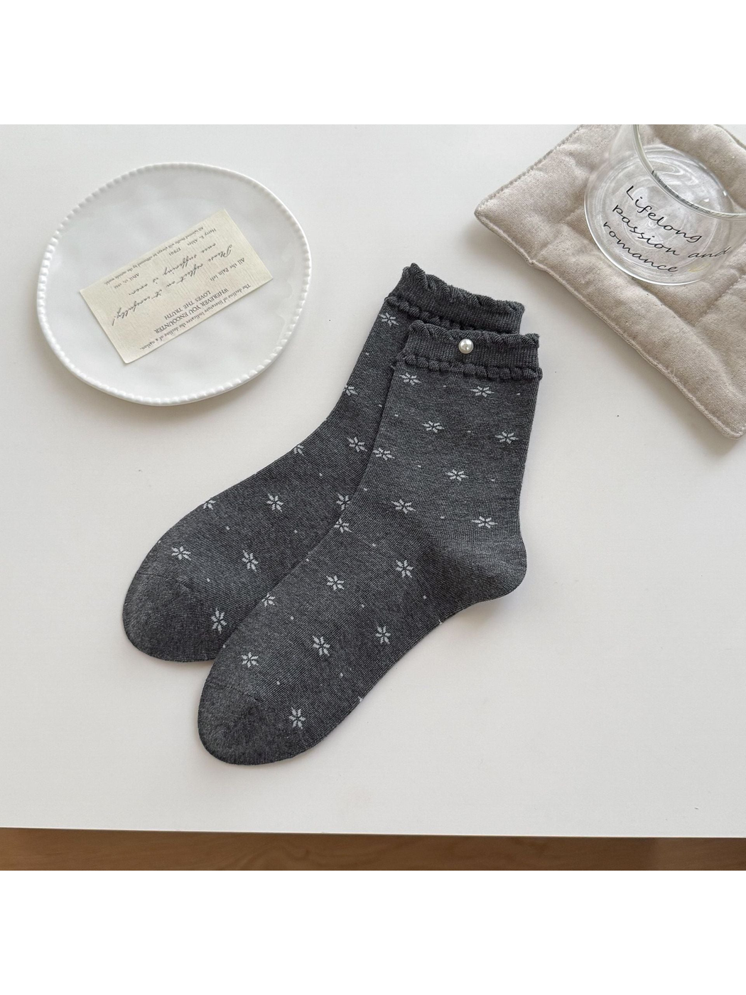 Dark Gray socks with pale floral motifs, ruffled cuffs and a round bead accent arranged on a tabletop.
