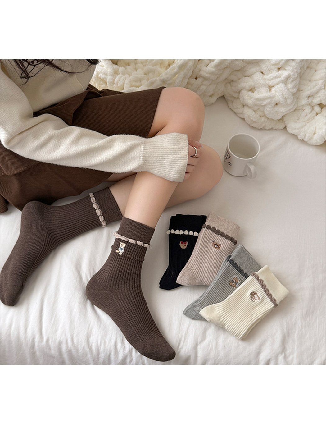 Coffee socks worn without shoes while seated beside folded Black, Beige, Gray, and Ivory socks.