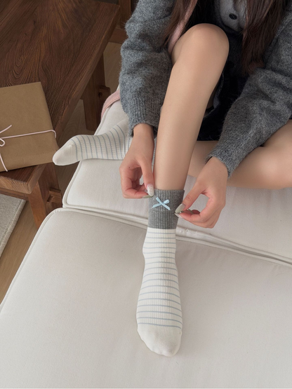 Hands adjust the gray ribbed cuff and pale blue bow of a striped sock.
