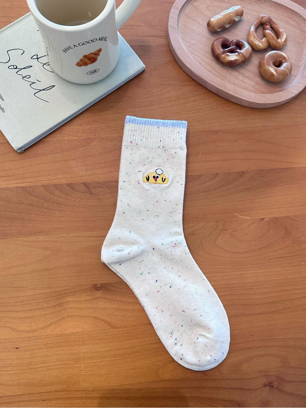Chef style ivory speckled sock with embroidered character and light blue cuff edge, laid flat.