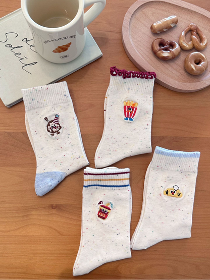 Folded ivory speckled socks displaying four embroidered food characters and contrasting cuff details.