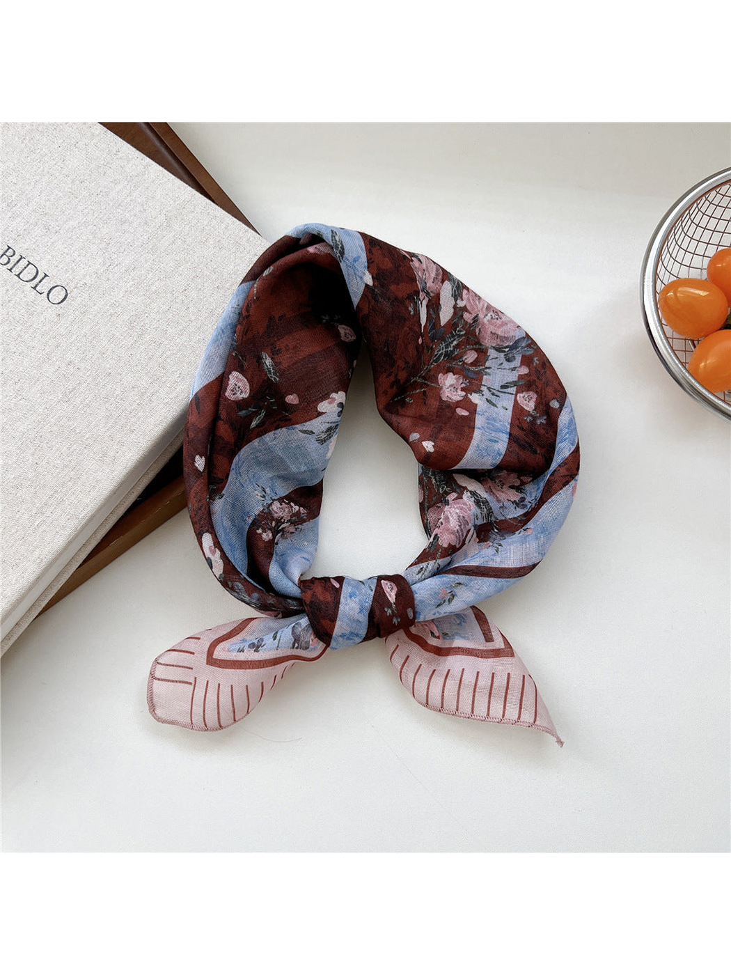 Blue Floral scarf tied in a loop with pink flowers across blue and brown bands.