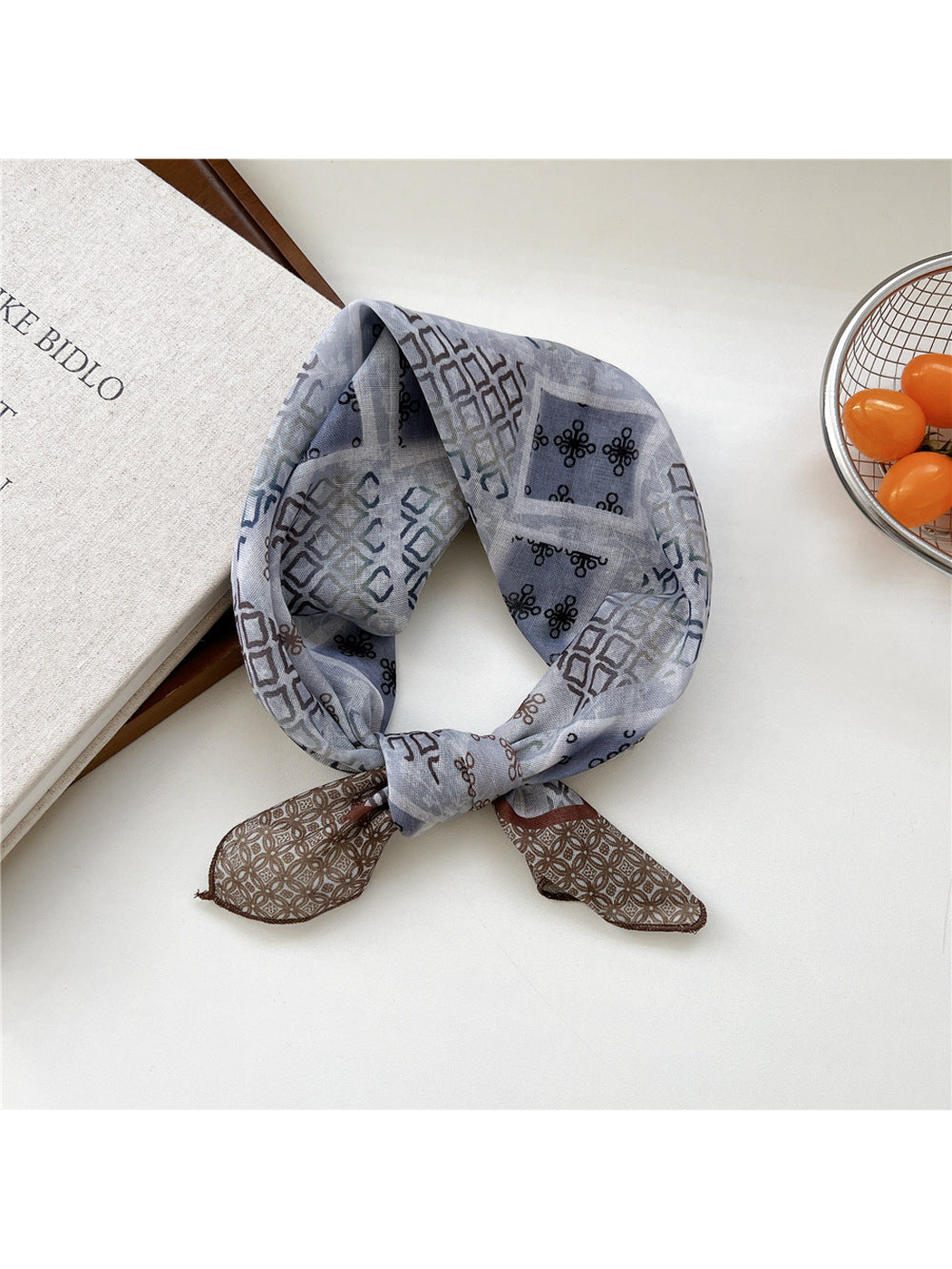 Geometric scarf tied in a loop with gray-blue patterned panels and brown lattice ends.