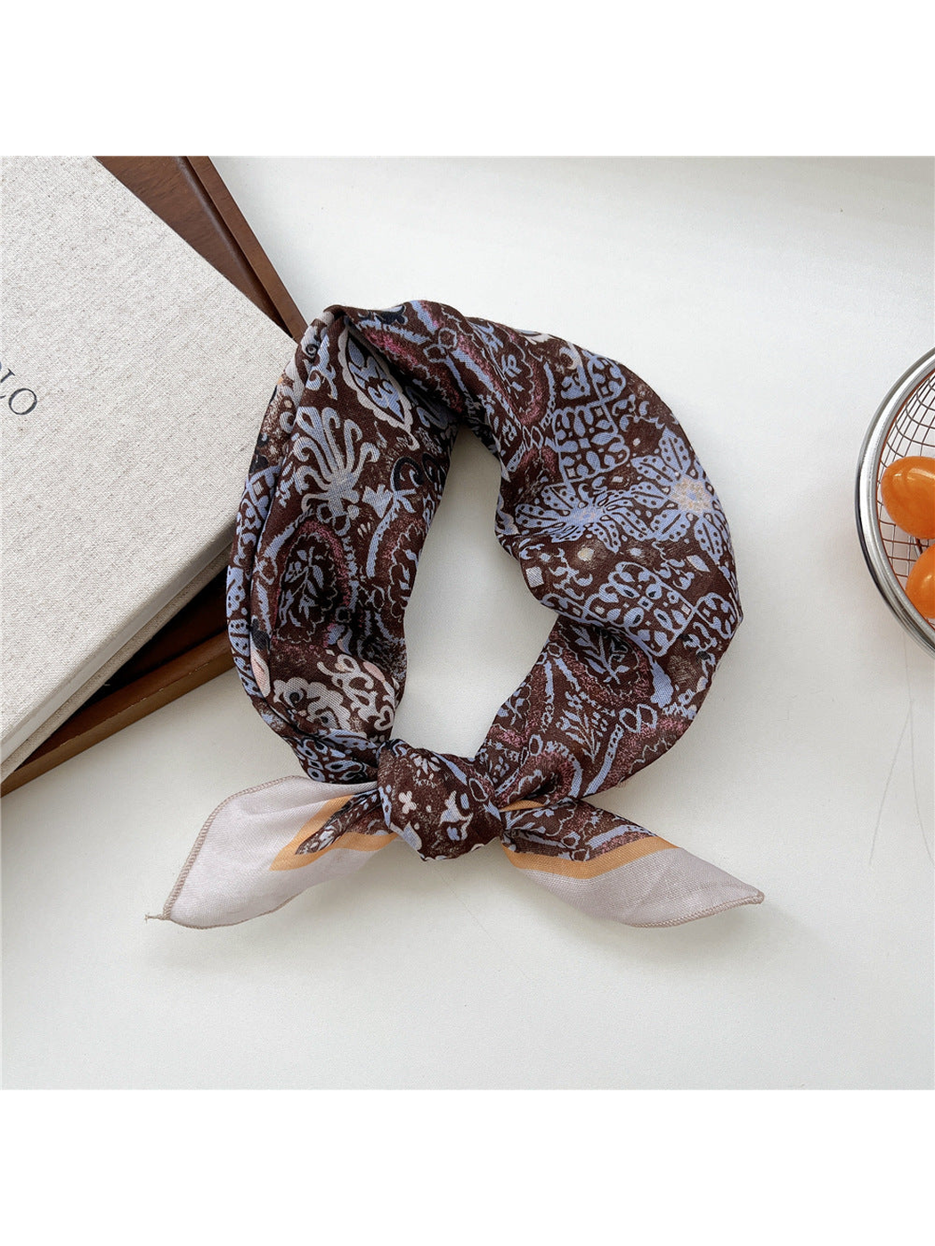 Abstract scarf tied in a loop with pale ornamental motifs on brown and a light border.