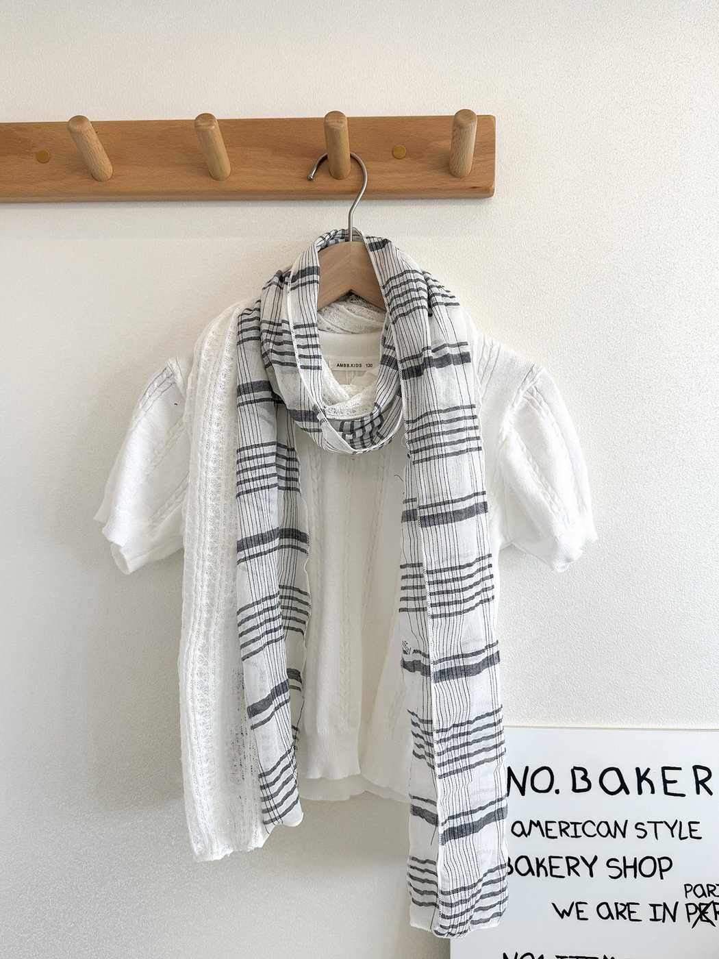 White plaid scarf with openwork panels looped over a white top on a hanger.