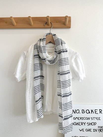 White plaid scarf with openwork panels looped over a white top on a hanger.