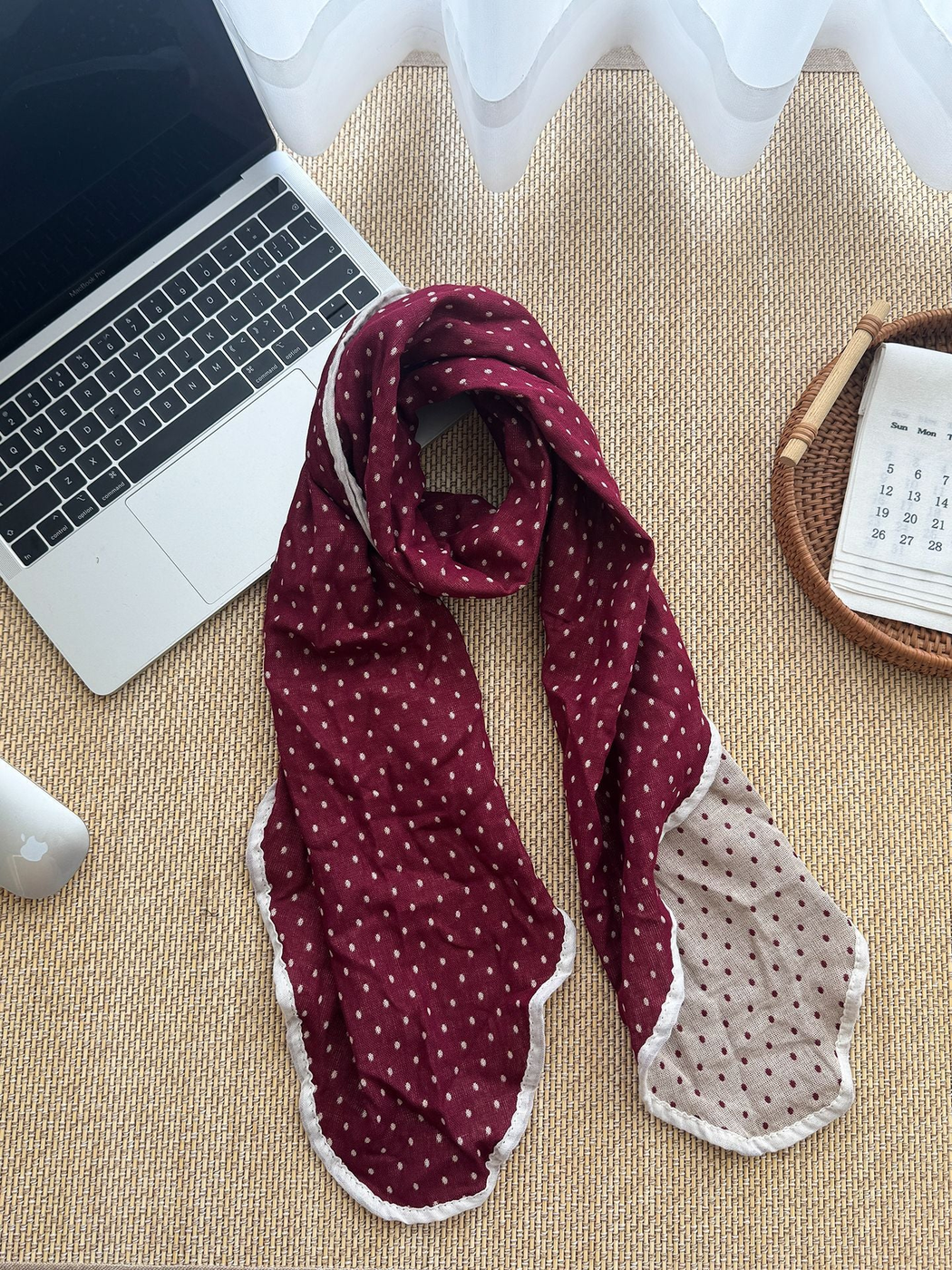 Burgundy polka dot scarf looped beside a laptop, with a pale reverse and contrasting edging visible.