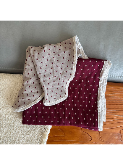Burgundy polka dot scarf folded to reveal its pale reverse, dotted pattern, and contrasting edge.