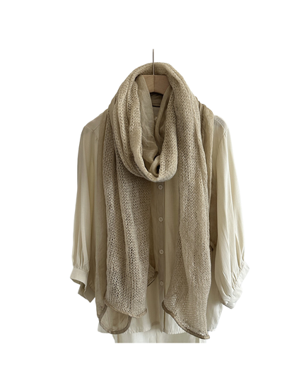 Beige scarf with openwork and sheer panels hanging in a long loop over a cream shirt.
