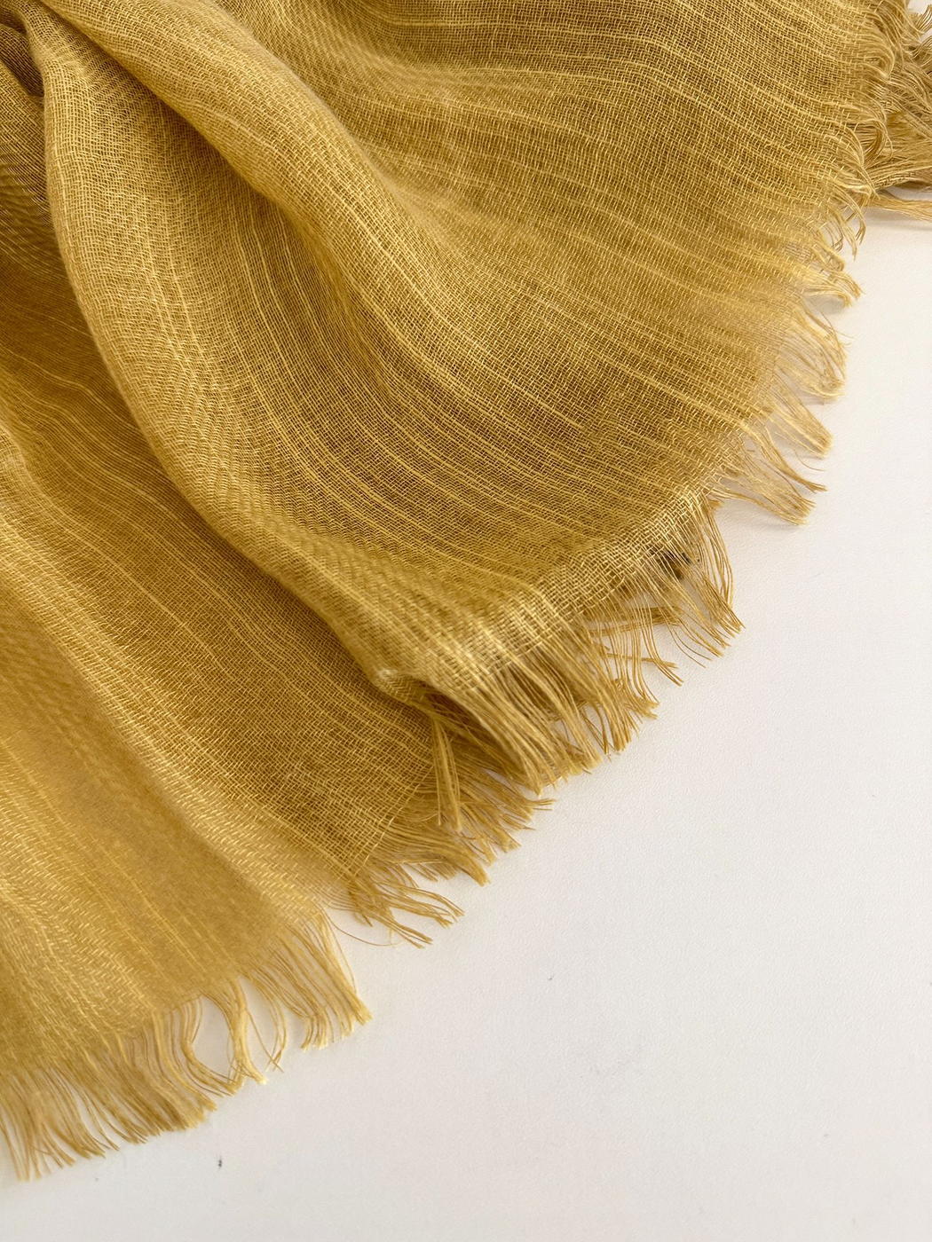 Close-up of the Mustard Yellow scarf's open weave and fine fringe against a pale background.
