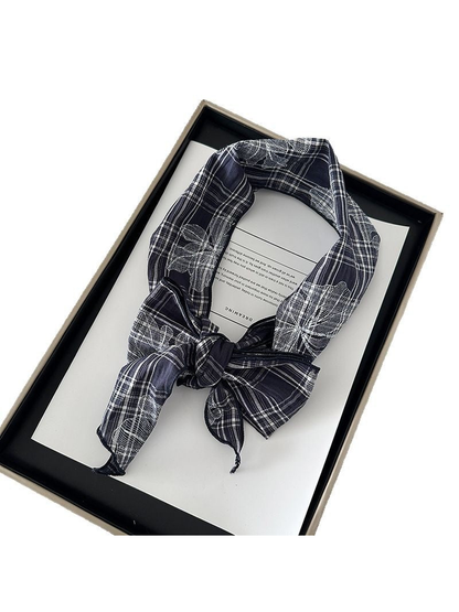 Navy plaid scarf with contrasting floral outlines tied in a bow on a display tray.