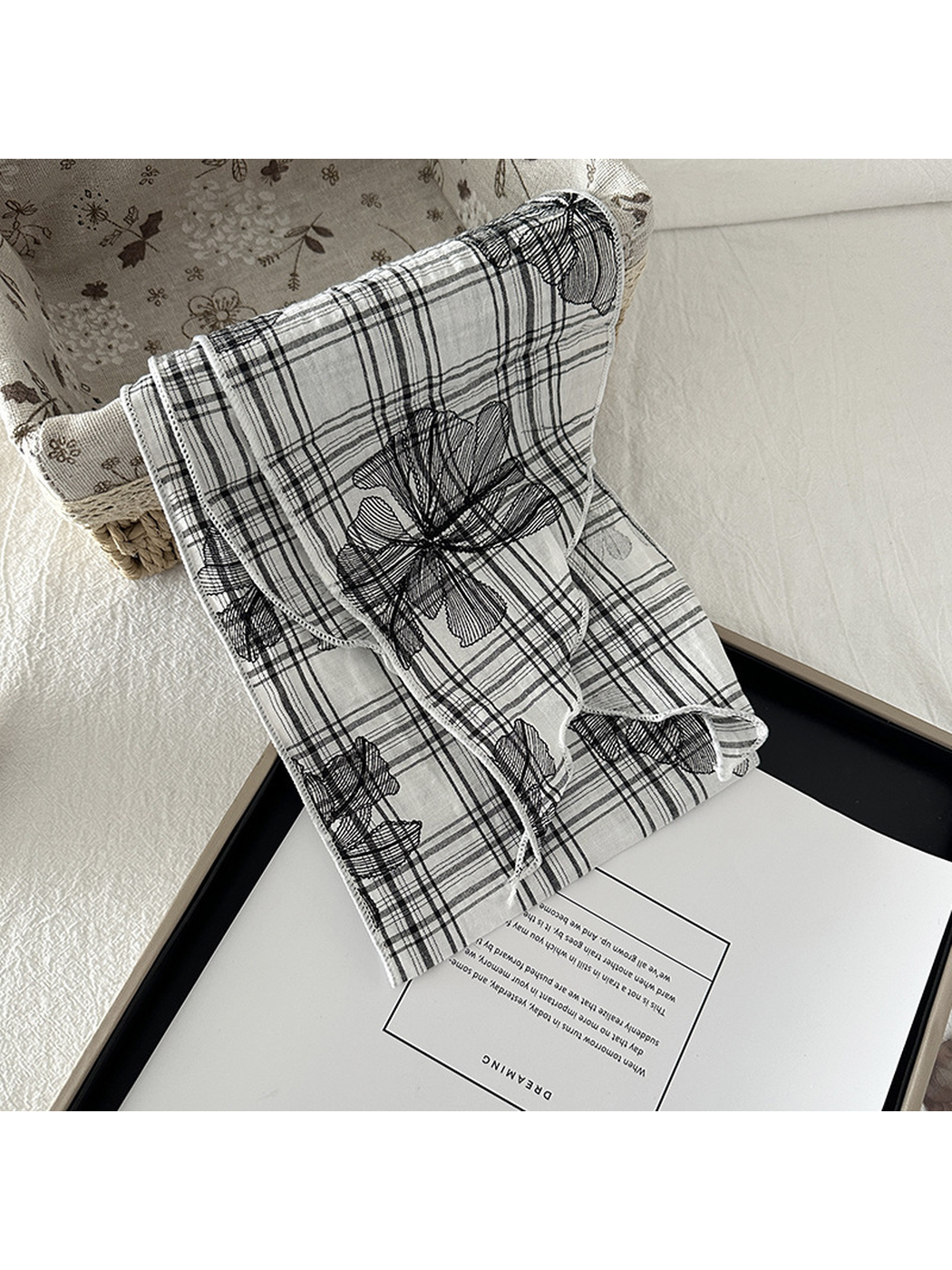 White floral plaid scarf draped over a basket edge, showing overlapping folds and tapered ends.