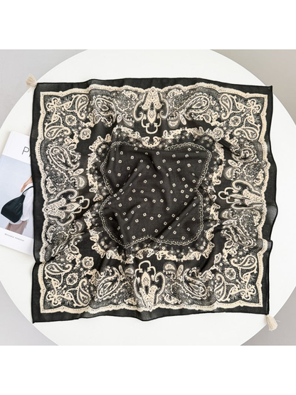 Square scarf spread flat with a cream paisley border, small central motifs, and corner tassels.