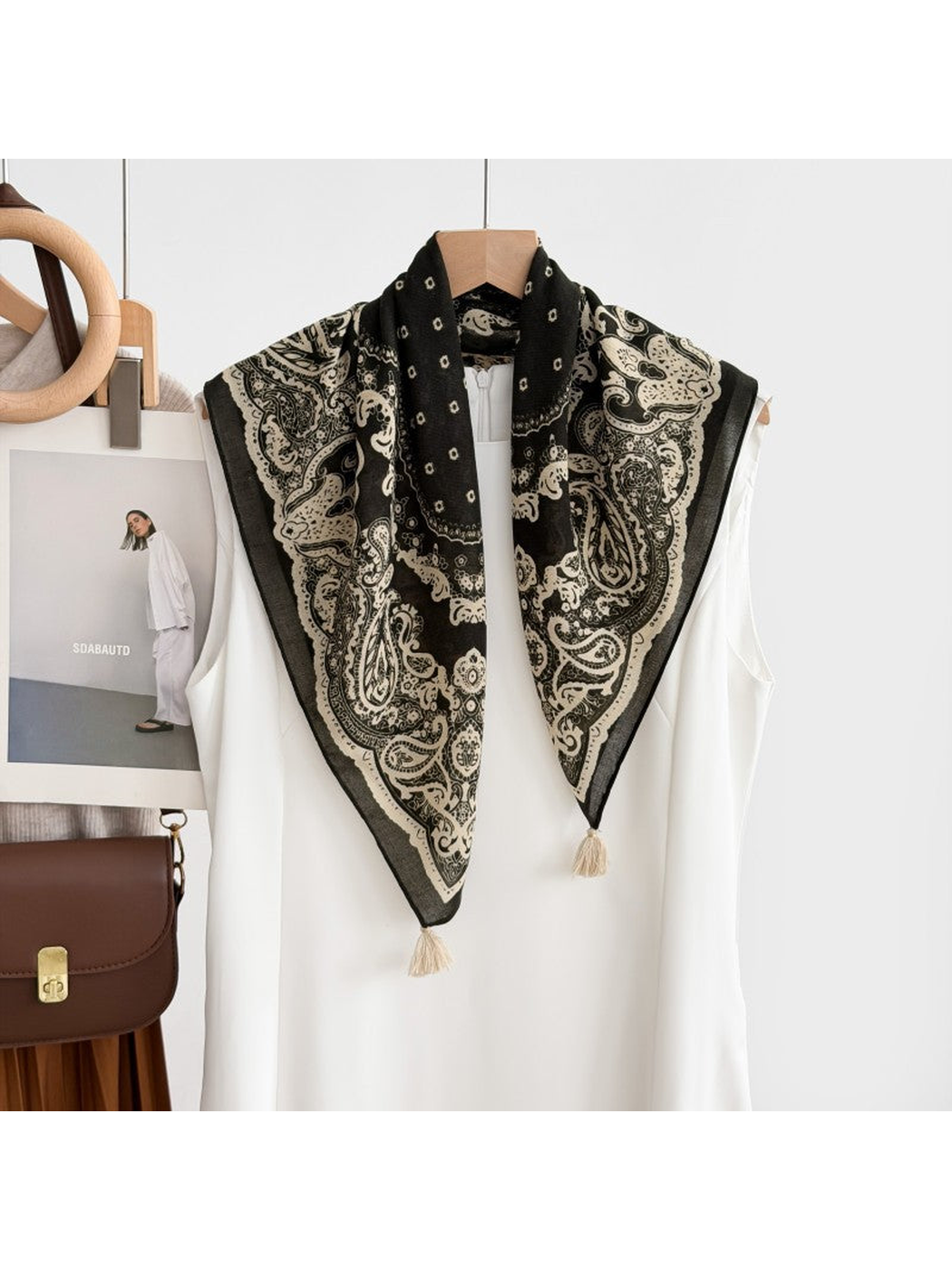 Paisley scarf with cream corner tassels draped over a white sleeveless garment on a hanger.
