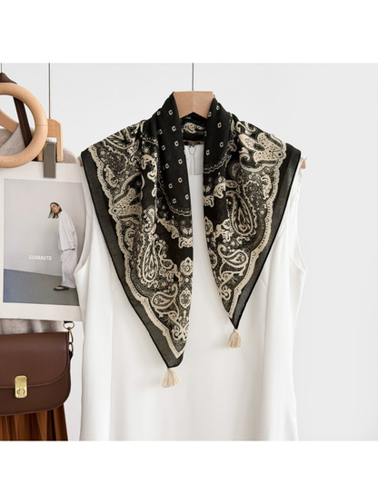 Paisley scarf with cream corner tassels draped over a white sleeveless garment on a hanger.