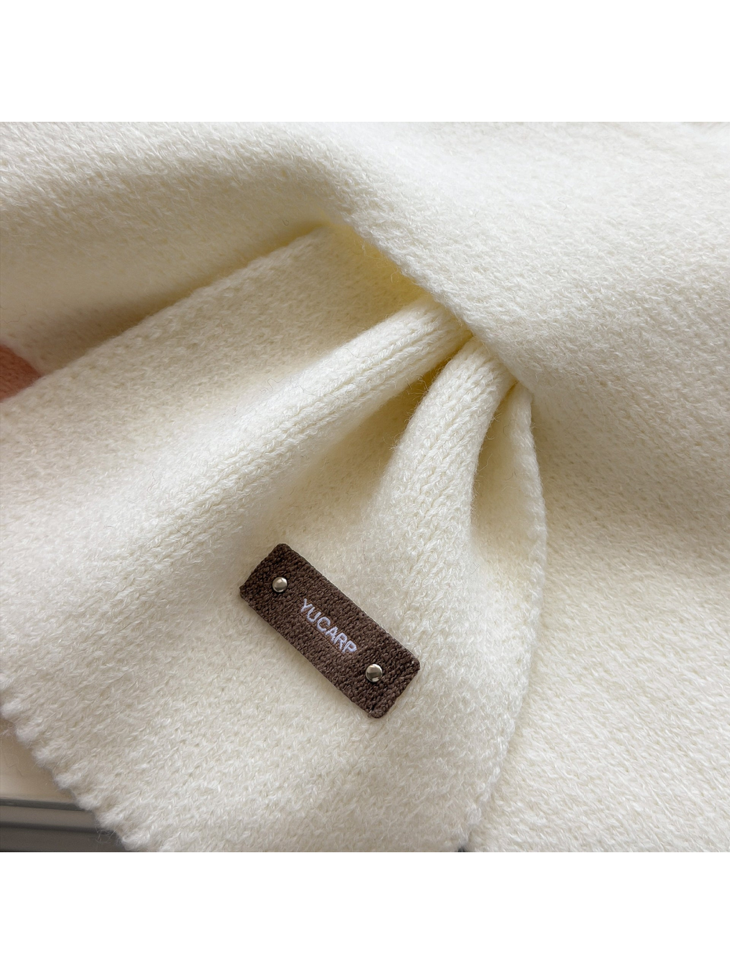 Close-up of Ivory scarf knit texture, pull-through fold and rectangular studded label.