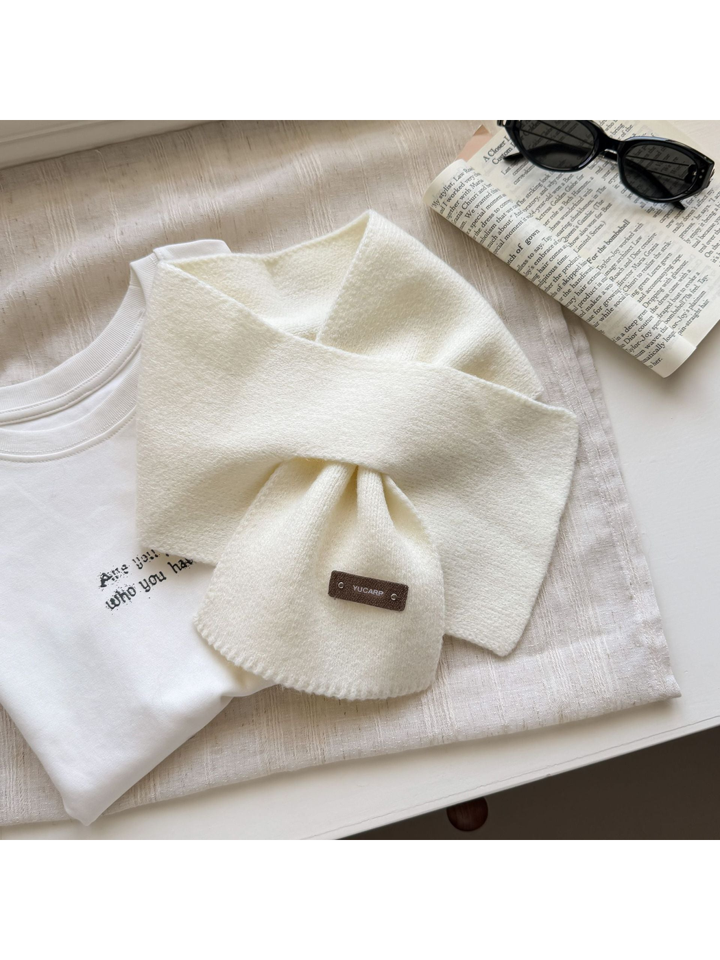 Ivory knit pull-through scarf with a rectangular label near one end.