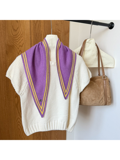 Purple knit triangle scarf with yellow border stripes and a round silver-tone charm draped over a white top.