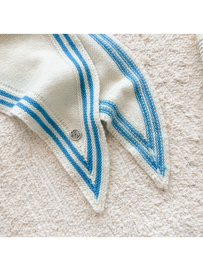 Close-up of an Ivory scarf's blue striped border, knit texture and round silver-tone charm.