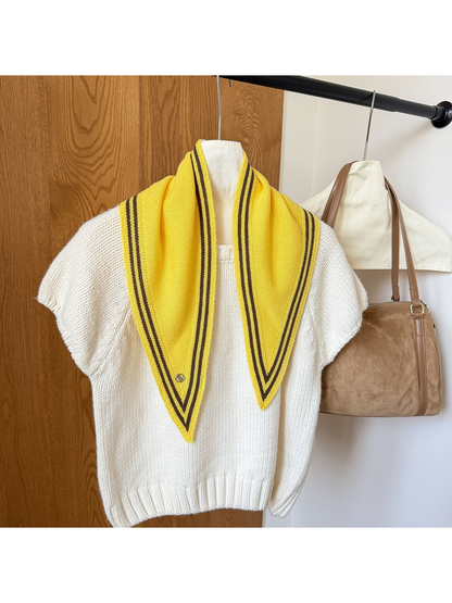 Yellow knit triangle scarf with brown border stripes draped over a white top.
