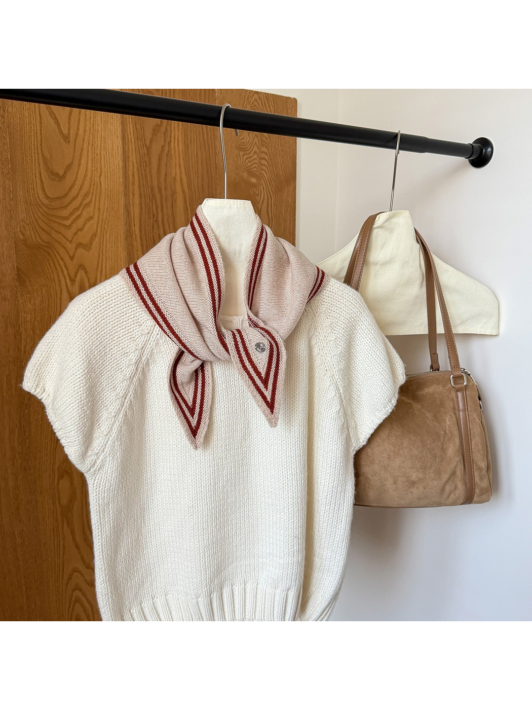 Beige knit triangle scarf with burgundy border stripes tied around the neckline of a white top.