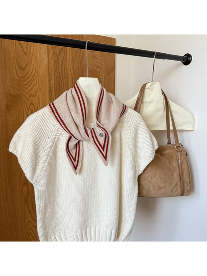 Beige knit triangle scarf with burgundy border stripes tied around the neckline of a white top.