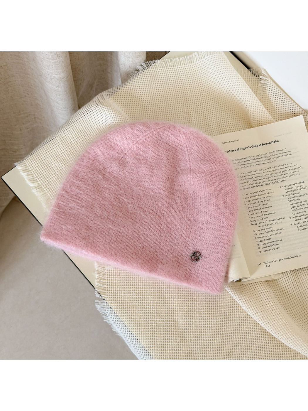 Light Pink fuzzy knit beanie with visible crown seams and a small silver-tone emblem near the lower edge.